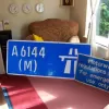 The four items safely stored indoors and looking larger than life. Closer inspection of the back of the start-of-restrictions signs reveal that it was manufactured in 1987 and is therefore original to the road: the only A6144(M) sign ever. Mission accomplished!