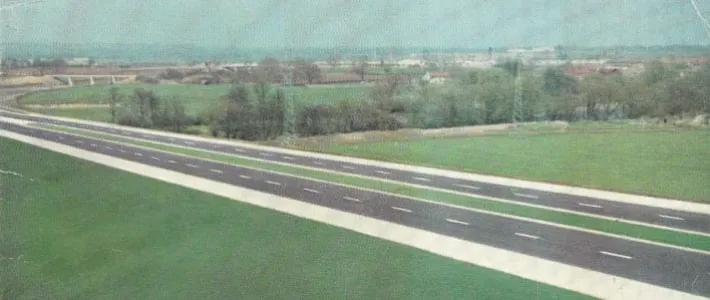 Colour photograph of an empty two-lane motorway passing ruler-straight through green countryside