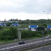From the northern end of the bridge, the gantry signs poking up above the trees hint at the enormous scale of this junction: the two signs are identical and stand side by side, each serving four lanes of traffic heading in the same direction.